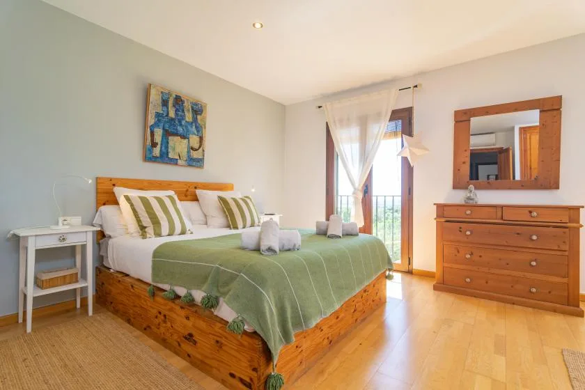 Un dormitorio con una cama de madera, ropa de cama verde y una cómoda junto a una ventana luminosa.