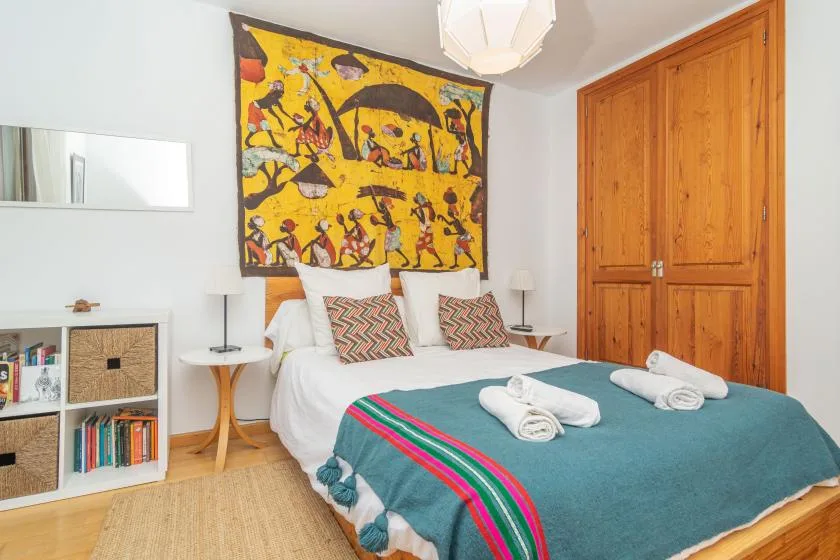 Un dormitorio con una cama vestida con ropa de cama color turquesa bajo un tapiz colorido.