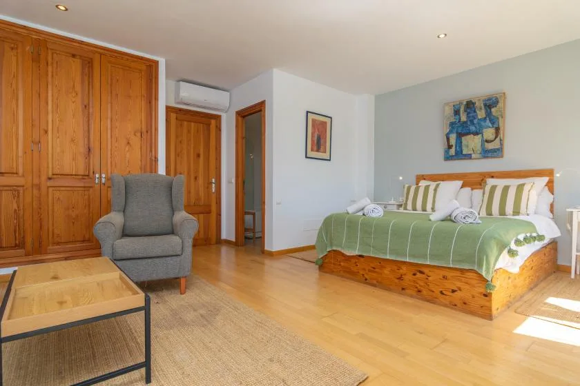 Un dormitorio con una cama de madera, almohadas a rayas y un sillón gris.