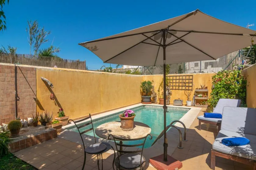 Una pequeña piscina al aire libre con asientos de patio y una gran sombrilla.