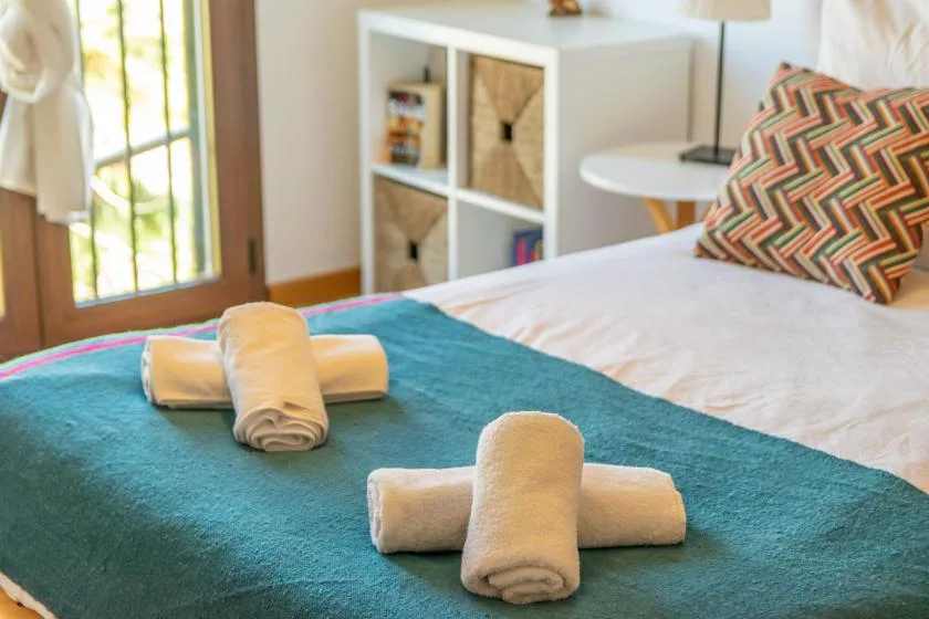 Un dormitorio con una cama cubierta por una manta turquesa y toallas dobladas.
