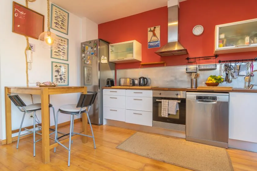 Una cocina con mesa de comedor, electrodomésticos de acero inoxidable y paredes rojas.