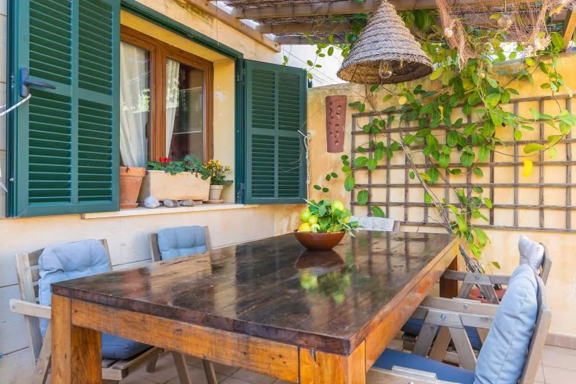 Una zona de comedor al aire libre con una mesa grande de madera y contraventanas verdes.