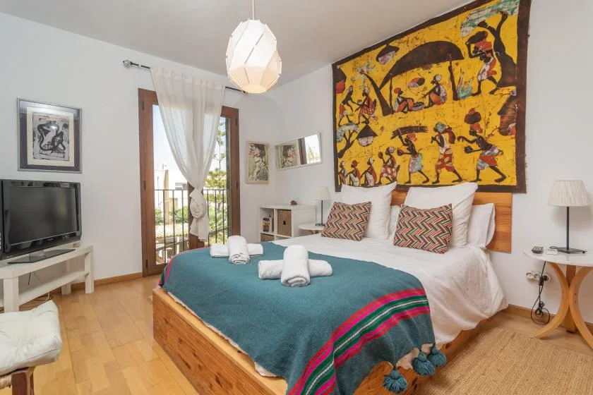Un dormitorio con una cama cubierta con ropa de cama verde azulado y arte colorido en la pared.