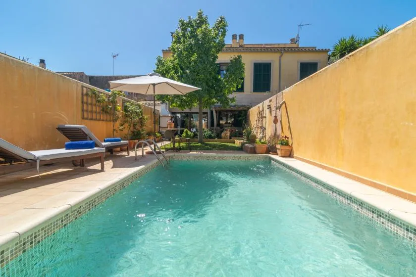 Una piscina de patio está entre tumbonas y una zona de estar con sombra.