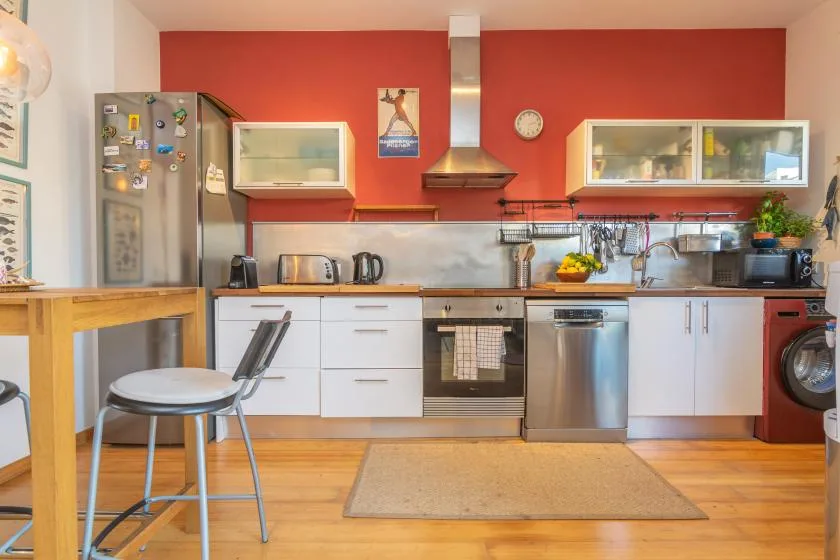 Una cocina con gabinetes blancos, una pared roja y piso de madera.