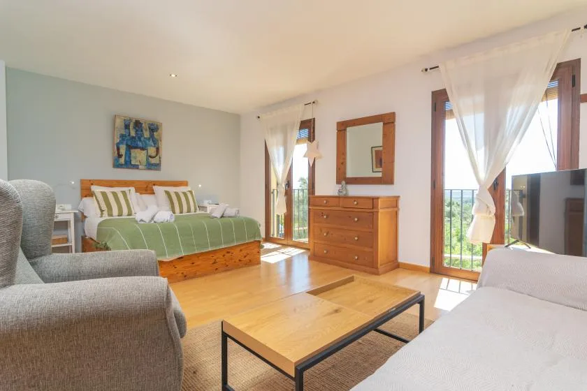 Un dormitorio luminoso con una cama verde, asientos y una mesa de centro de madera.