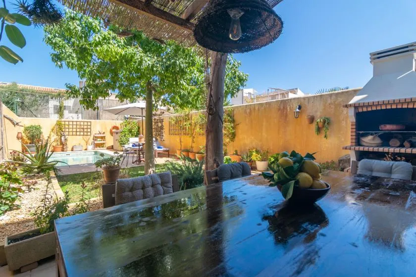 Un patio al aire libre con una mesa, plantas y una piscina al fondo.