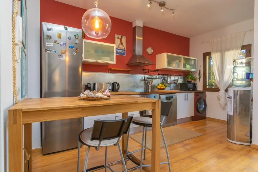 Una cocina con una mesa de madera, un refrigerador de acero inoxidable y paredes rojas.