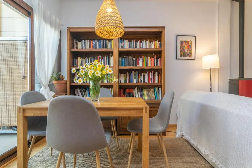 Comedor con una mesa de madera, sillas, flores y una estantería.