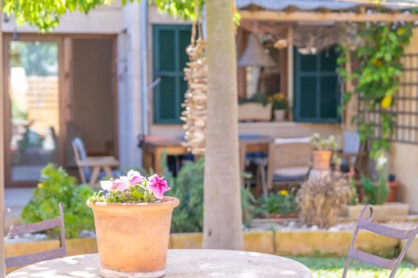 Un patio ajardinado con asientos al aire libre y una maceta con flores sobre una mesa.