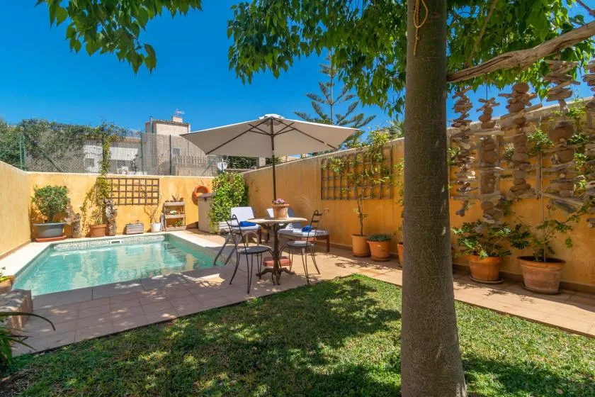 Un patio ajardinado con piscina, asientos al aire libre y una gran sombrilla.