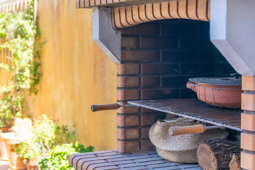Una parrilla exterior de ladrillo con una rejilla de cocción y utensilios.