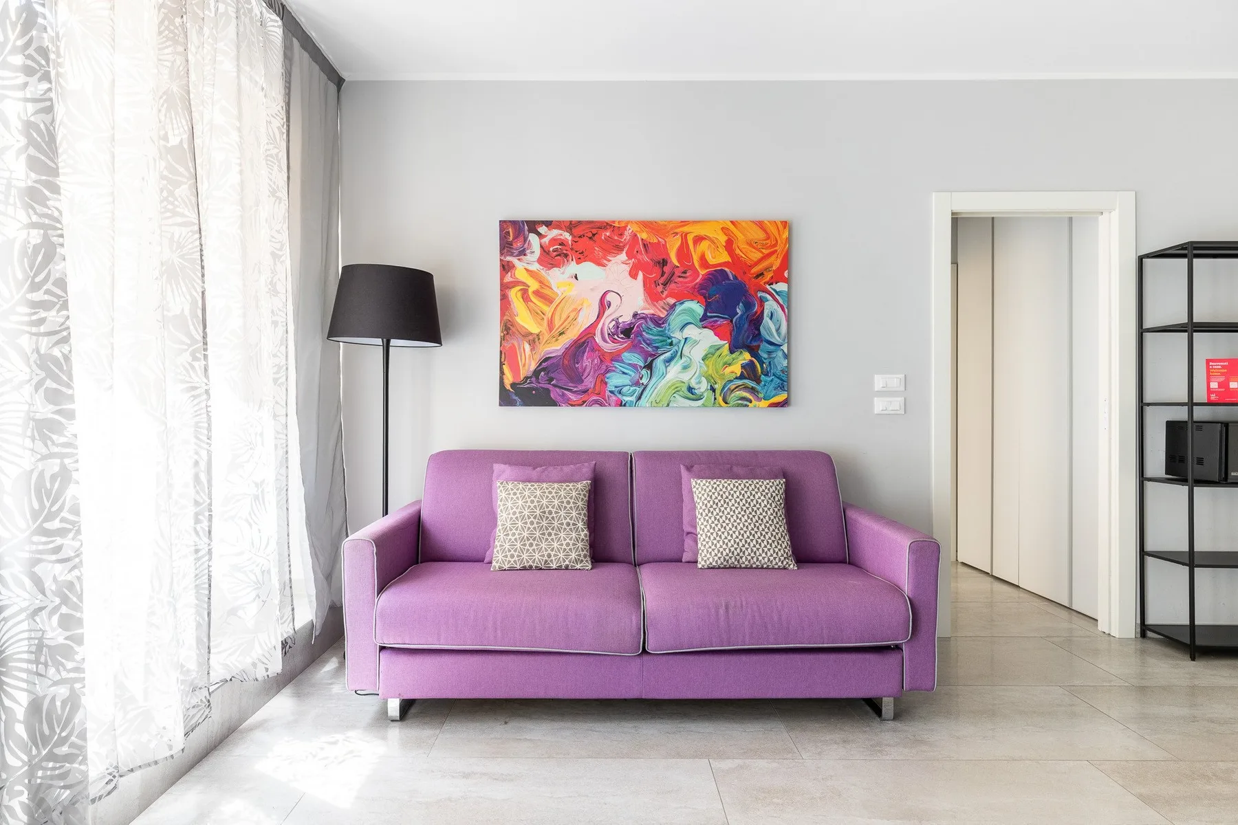 Una sala de estar con un sofá morado bajo una colorida pintura abstracta.