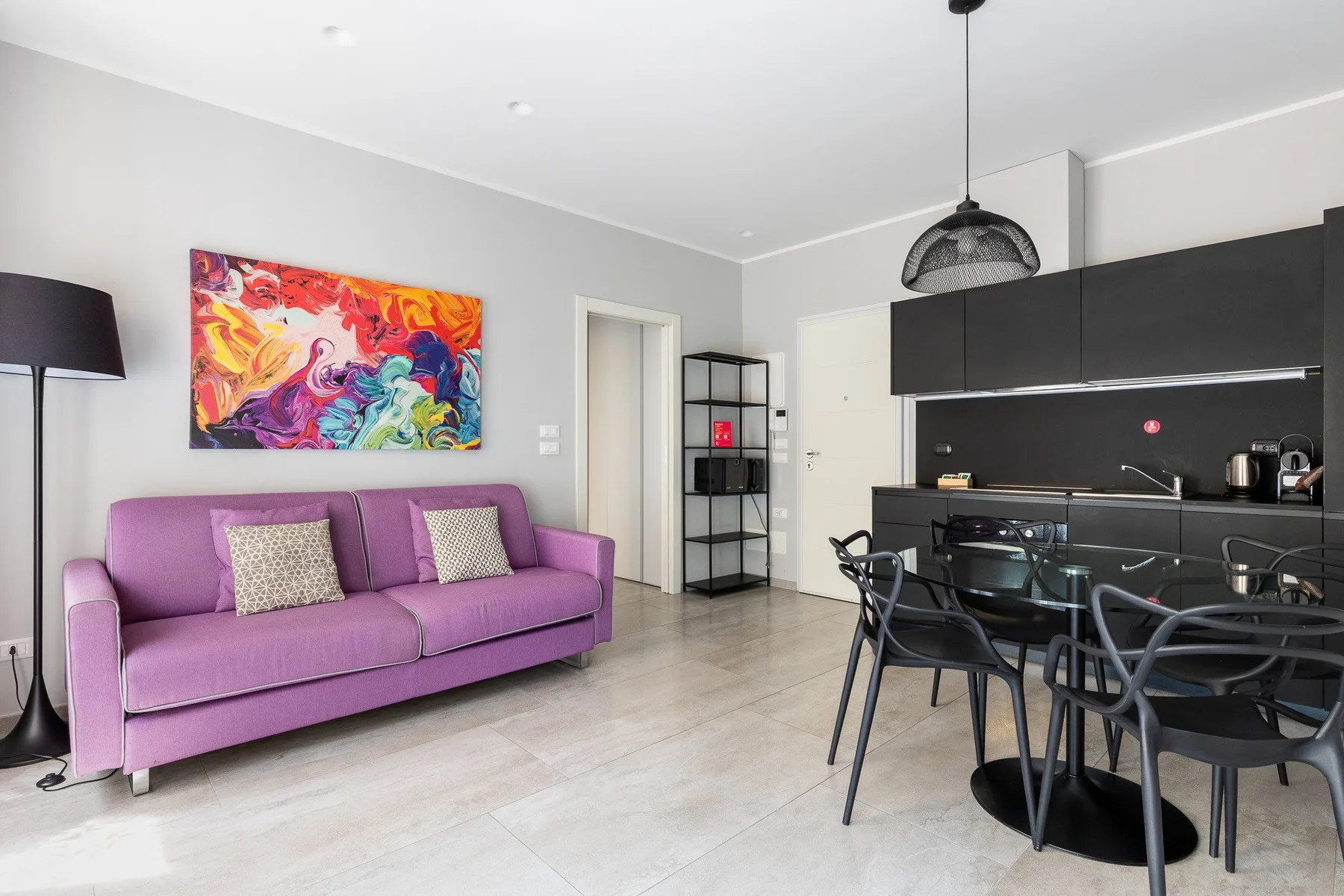 Una luminosa sala de estar y comedor con un sofá morado y gabinetes de cocina negros.