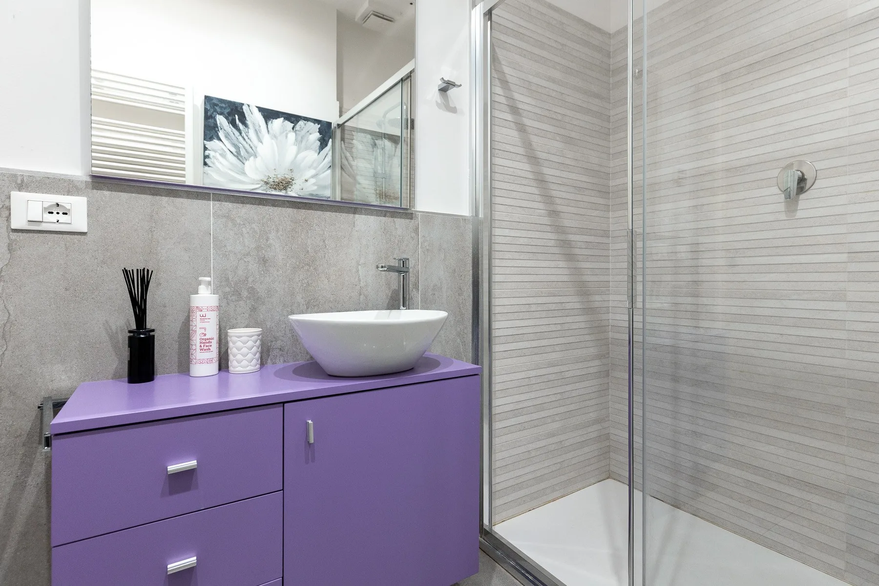 Un baño moderno con mueble morado, lavabo de recipiente y ducha de vidrio.