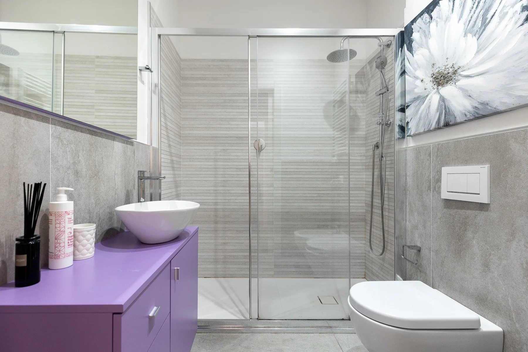 Un baño con ducha de vidrio, tocador morado e inodoro.