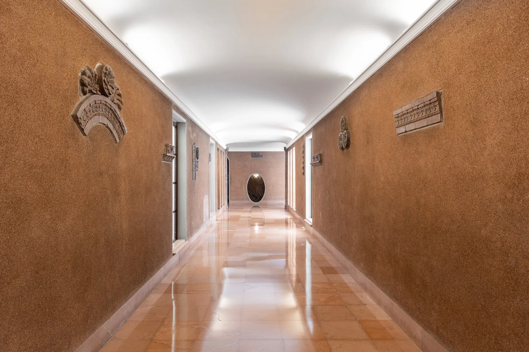 Un largo pasillo interior con paredes color terracota y suelo de baldosas reflectante.