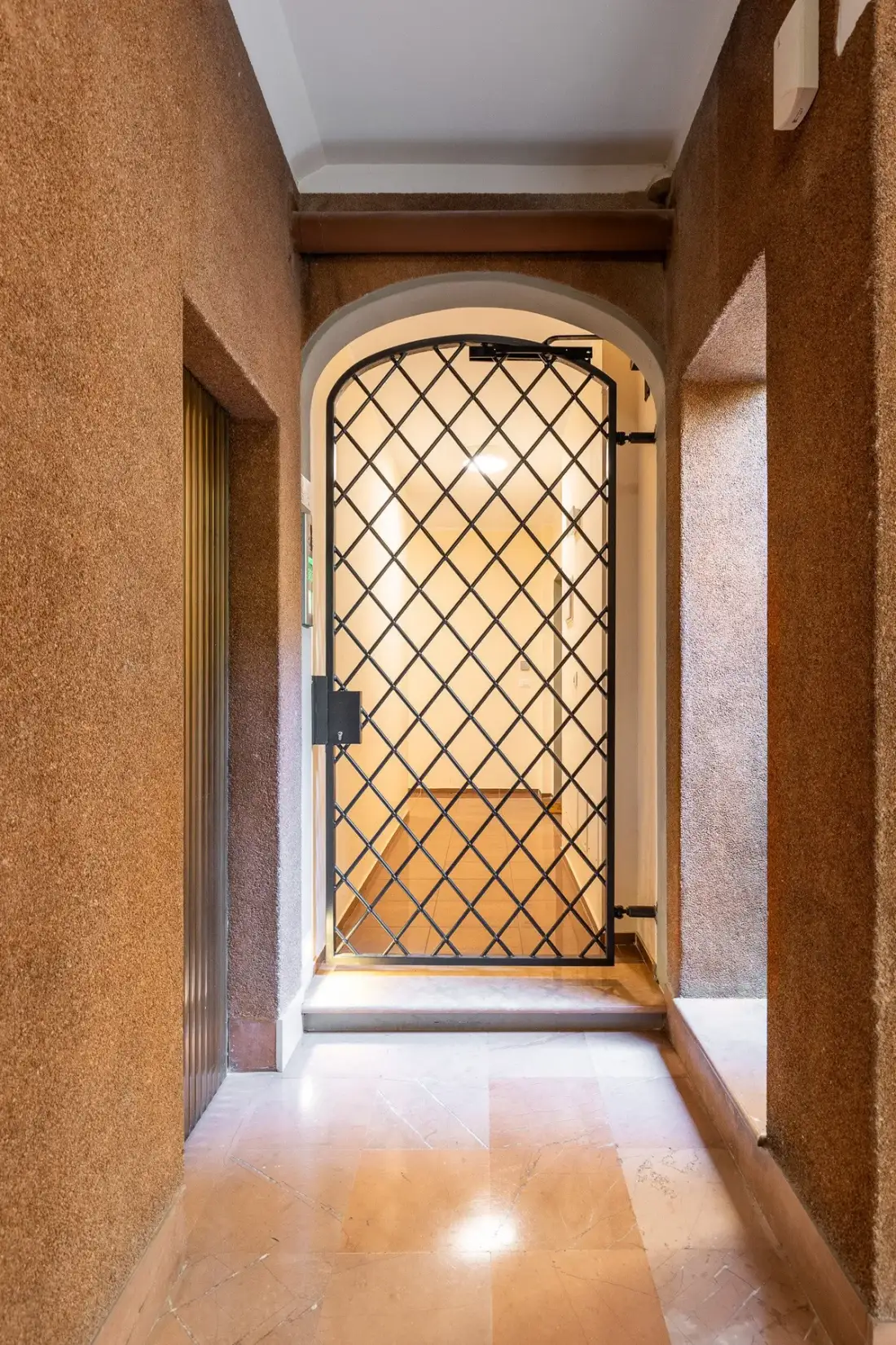 Un pasillo estrecho conduce a una puerta arqueada con una reja de metal oscuro.