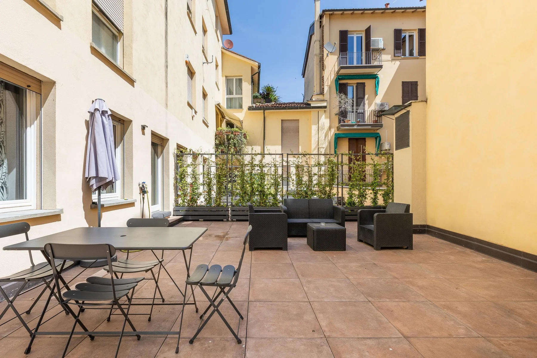 Una terraza soleada en un patio, con asientos al aire libre y plantas en macetas.