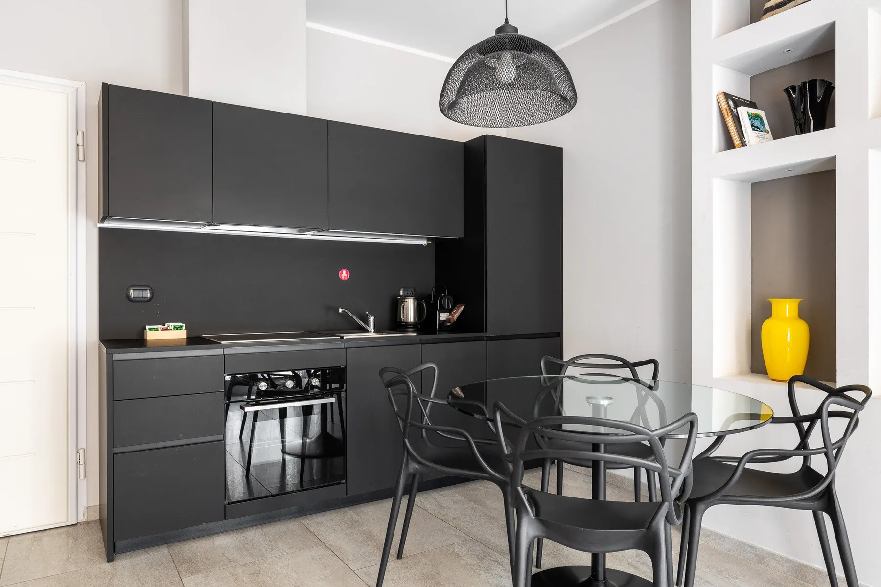 Una cocina moderna y zona de comedor con armarios oscuros y una mesa de cristal.