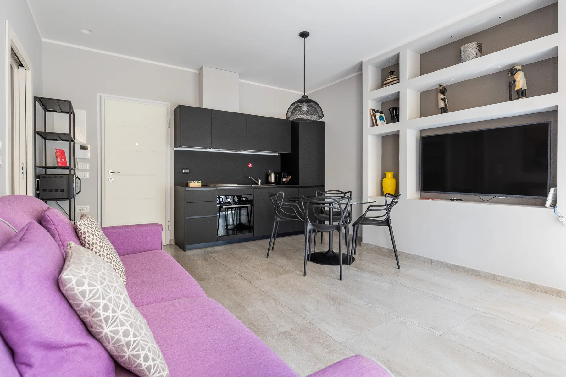 Una sala de estar con un sofá morado, una mesa de comedor y estantes empotrados para televisión.