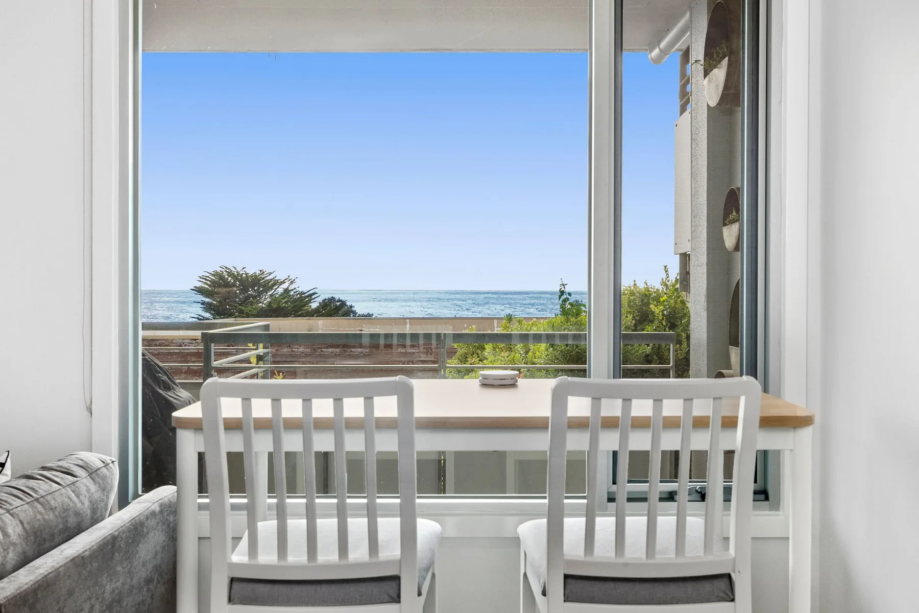 A dining table and chairs sit beside a large window overlooking the ocean.
