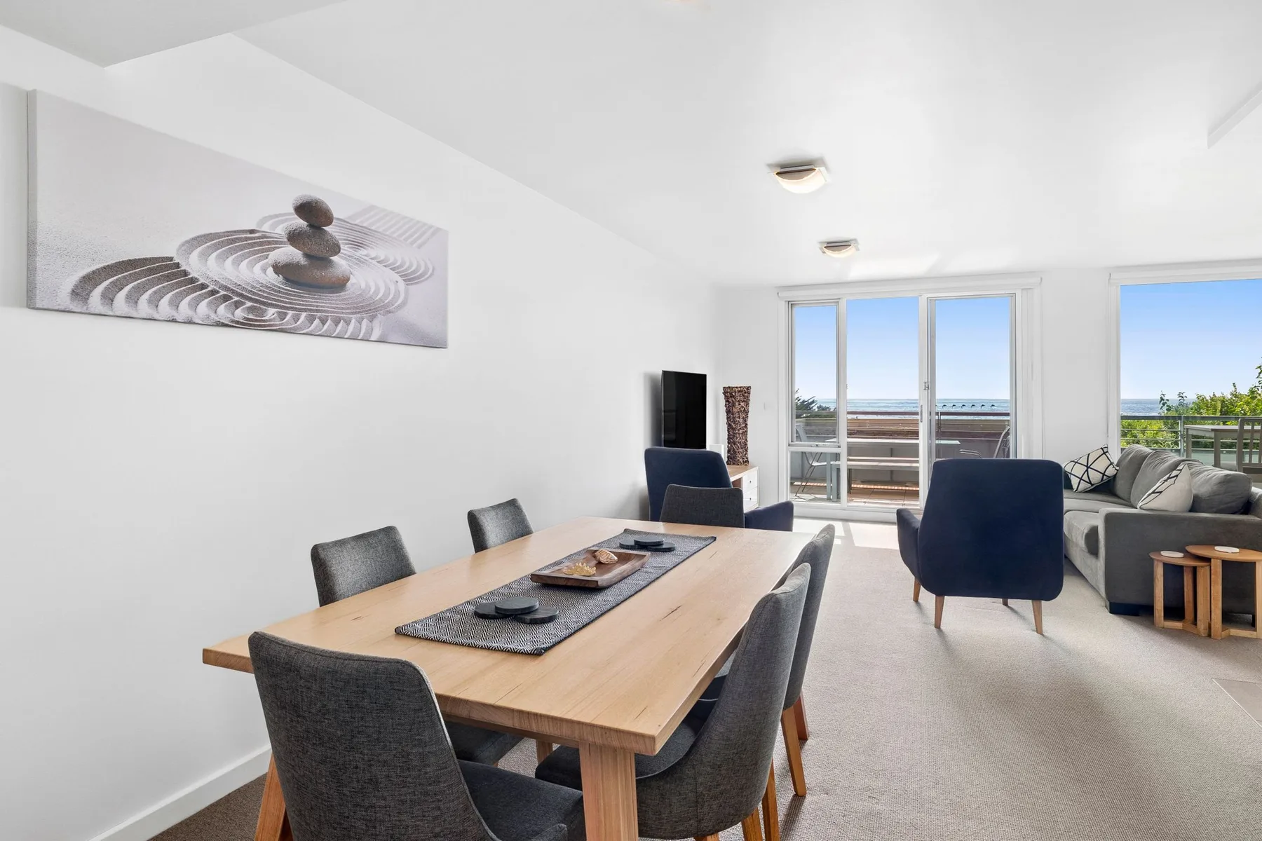 A bright living and dining area with a wooden table and seating by large windows.