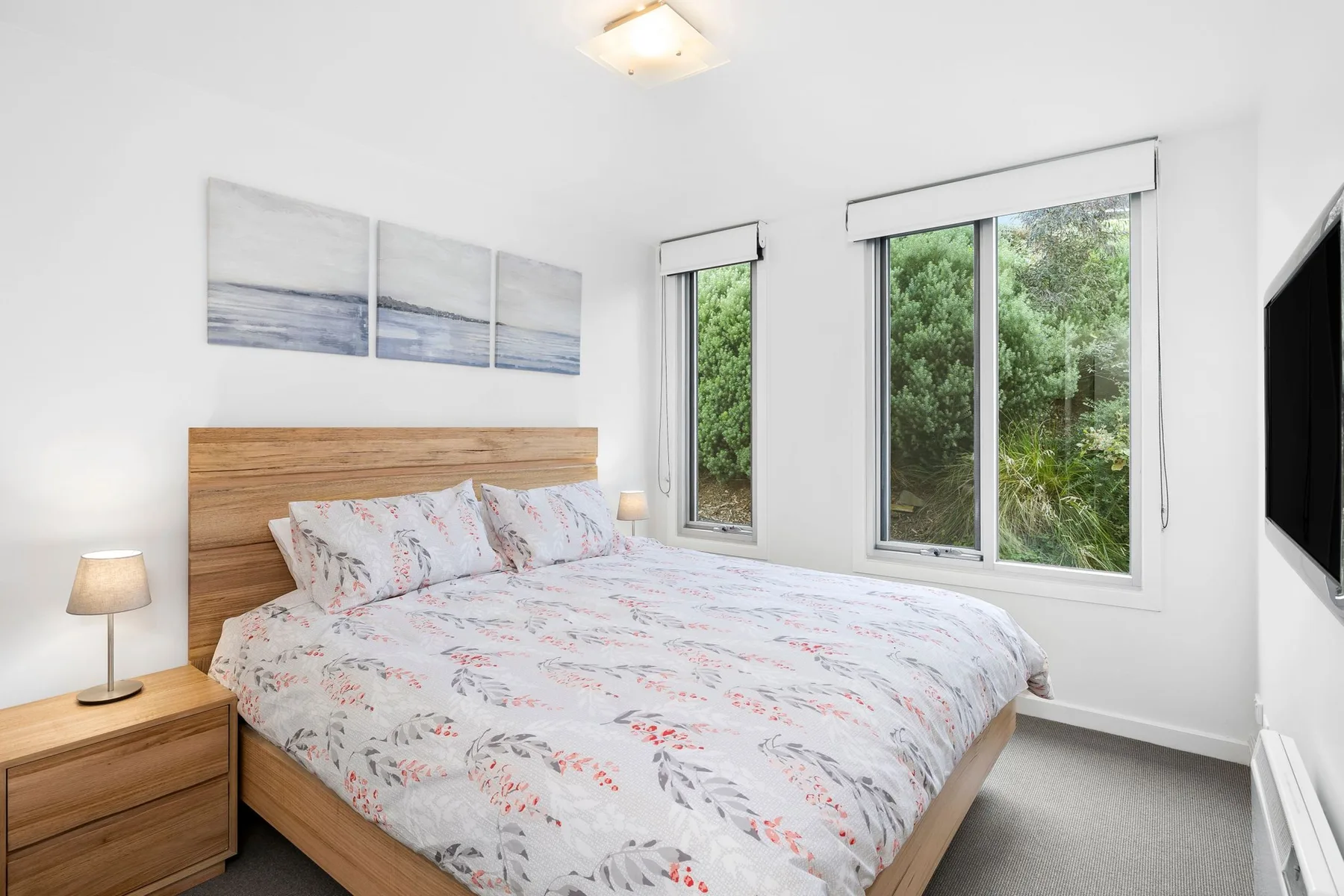 A bedroom with a bed beside large windows overlooking greenery.