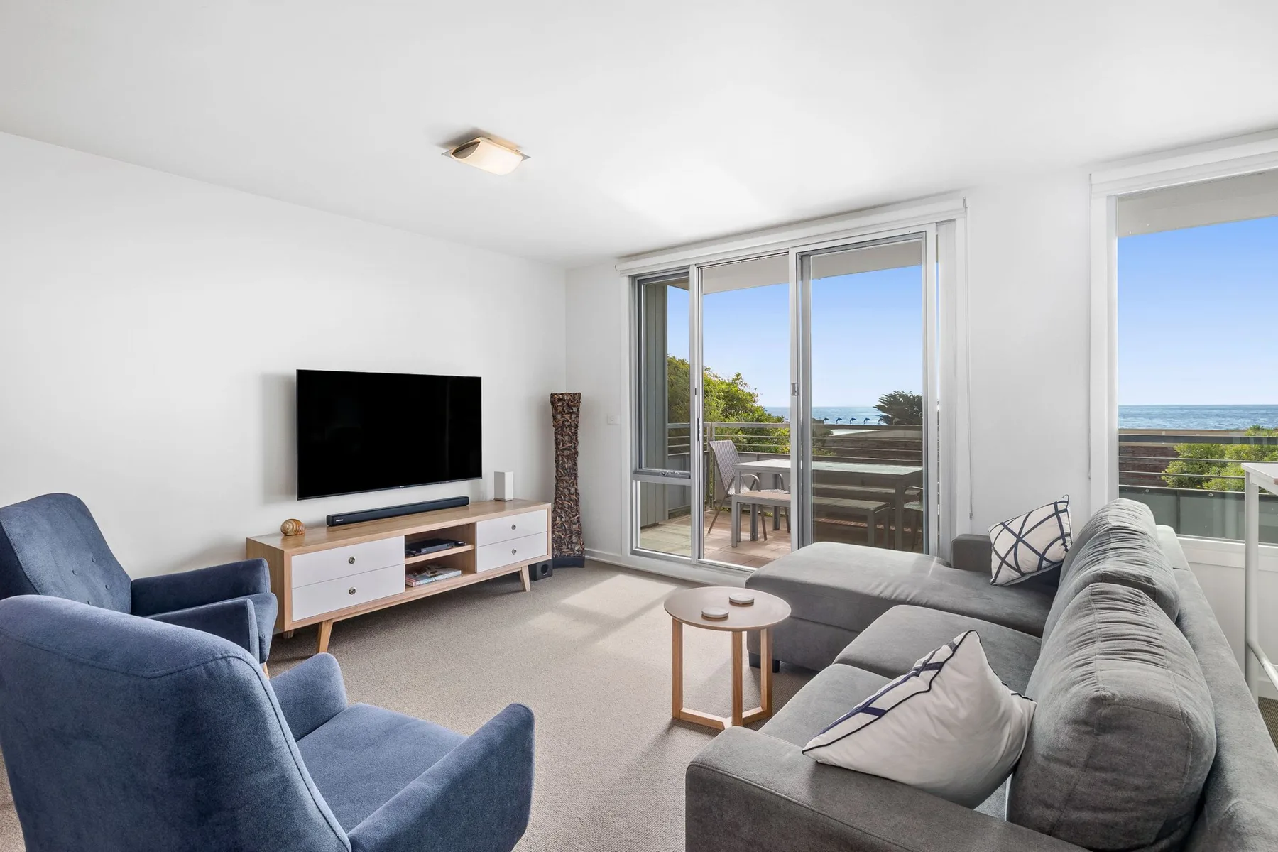 A bright living room with seating, a television, and large windows overlooking the water.