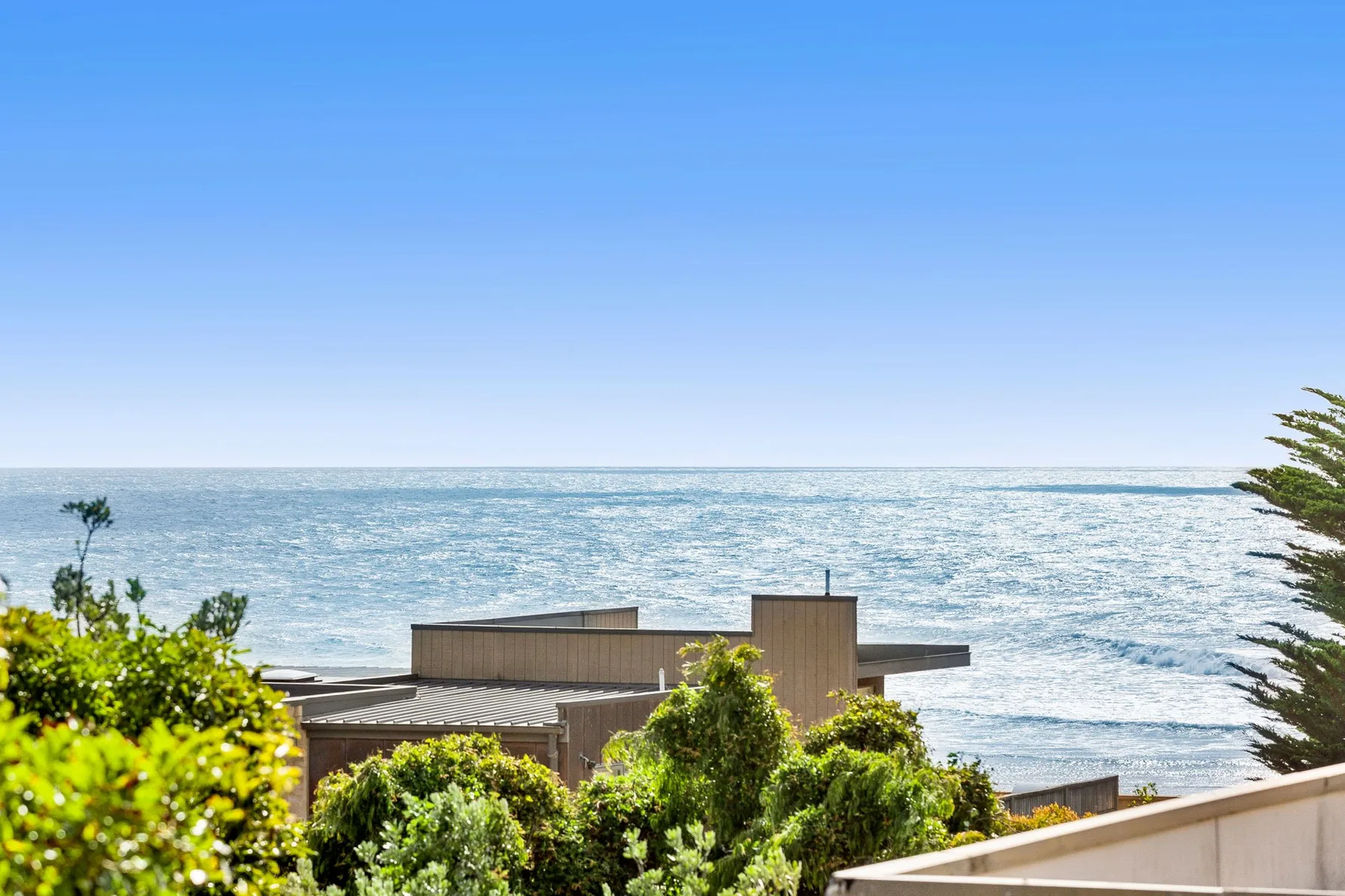 A coastal building sits behind leafy greenery, with the ocean visible beyond.