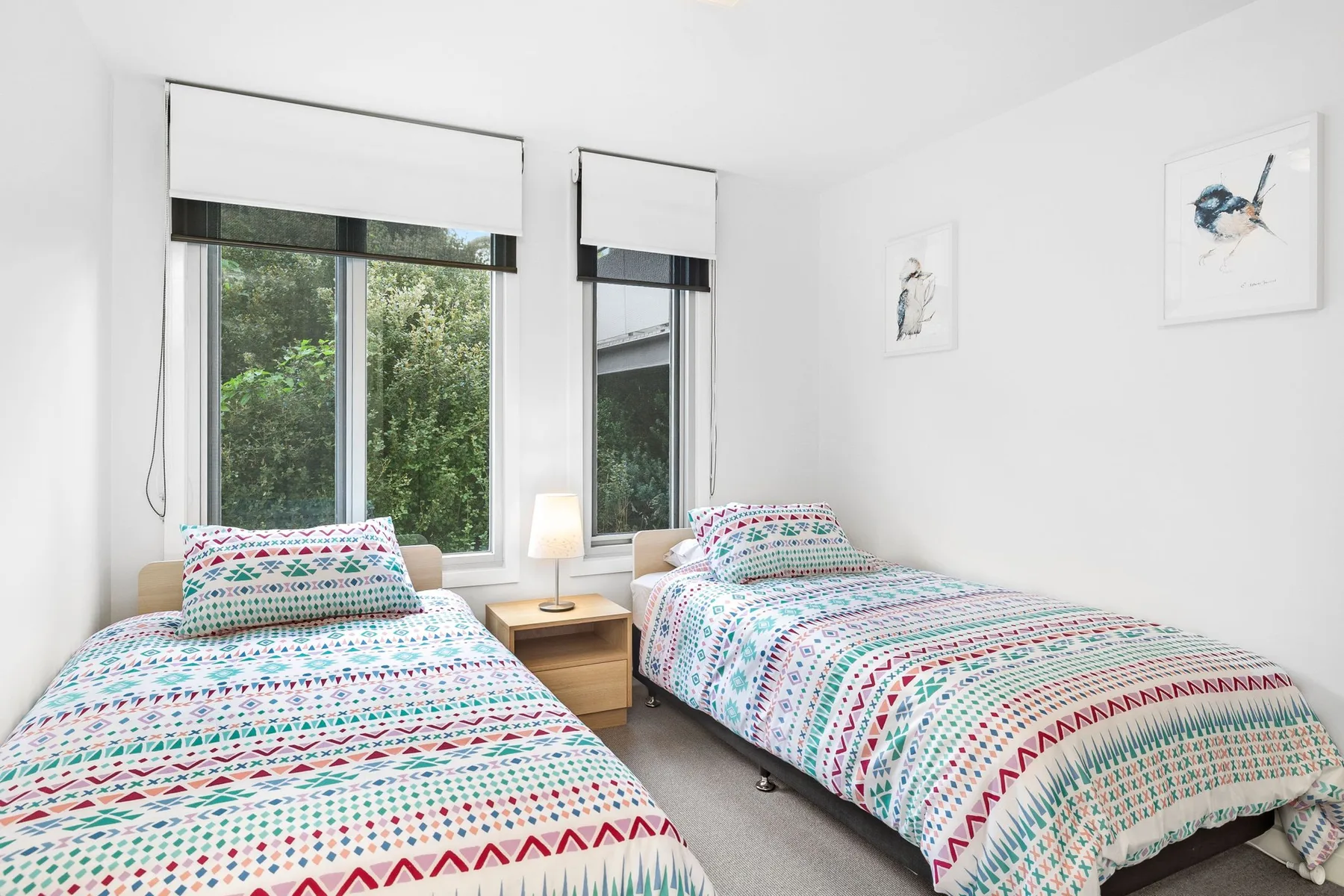A bright bedroom with two beds dressed in colorful patterned bedding.