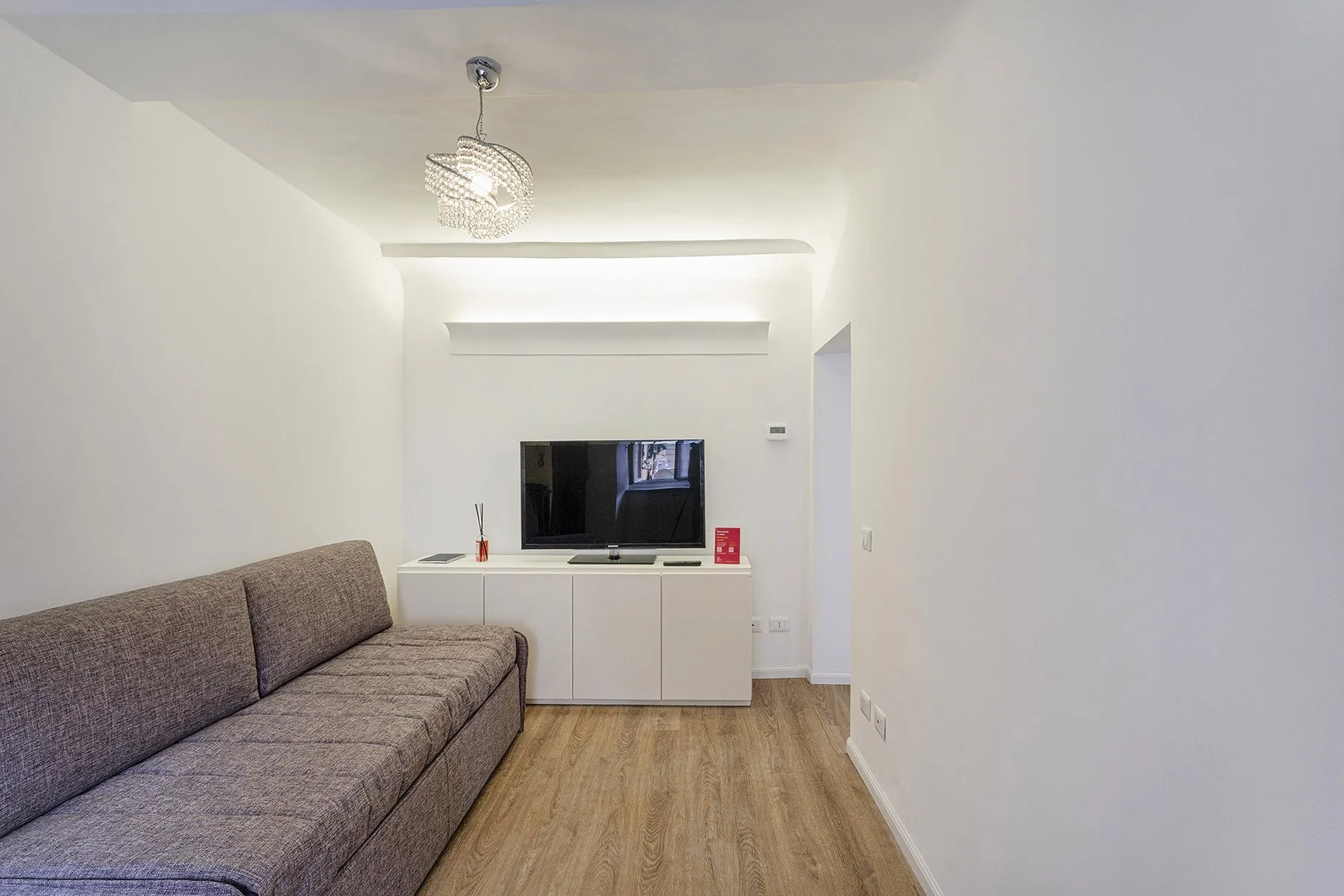 A small living room with a gray sofa facing a television on a low cabinet.