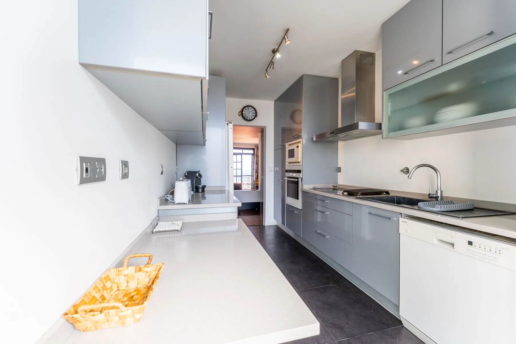 A modern kitchen with gray cabinets, a long counter, and a sink.