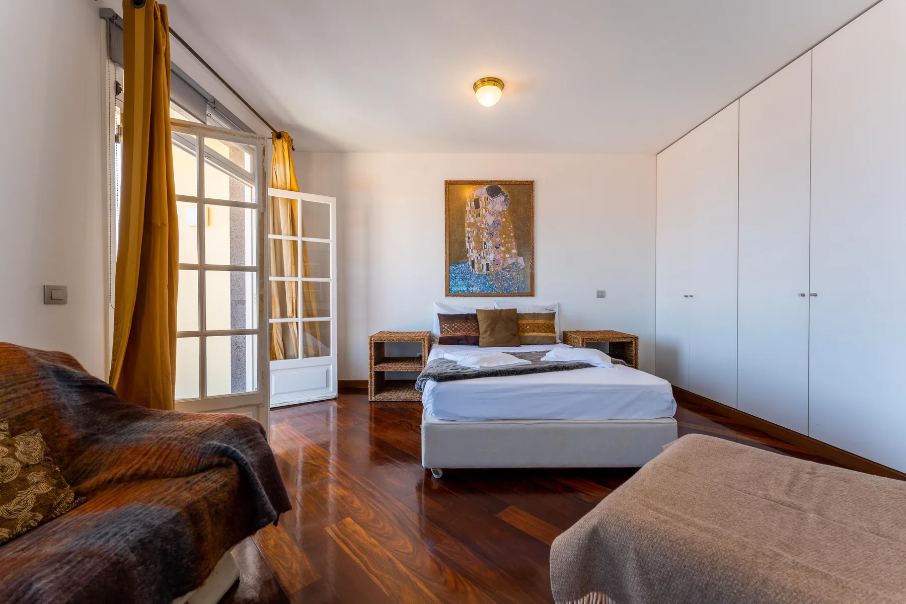 A bedroom with a bed, seating, and tall white wardrobes.