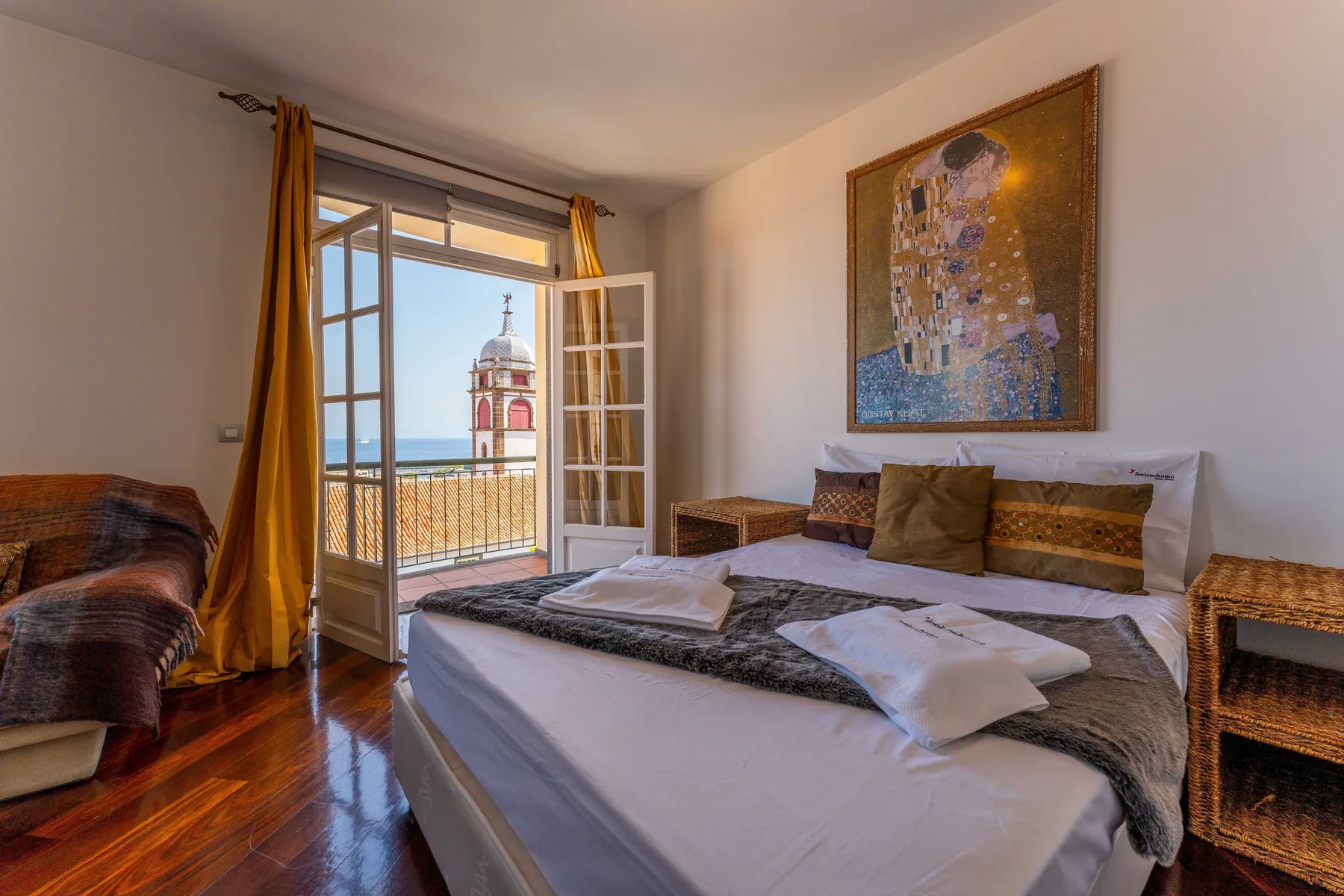 A bedroom with a bed, a wall painting, and open doors to a balcony.