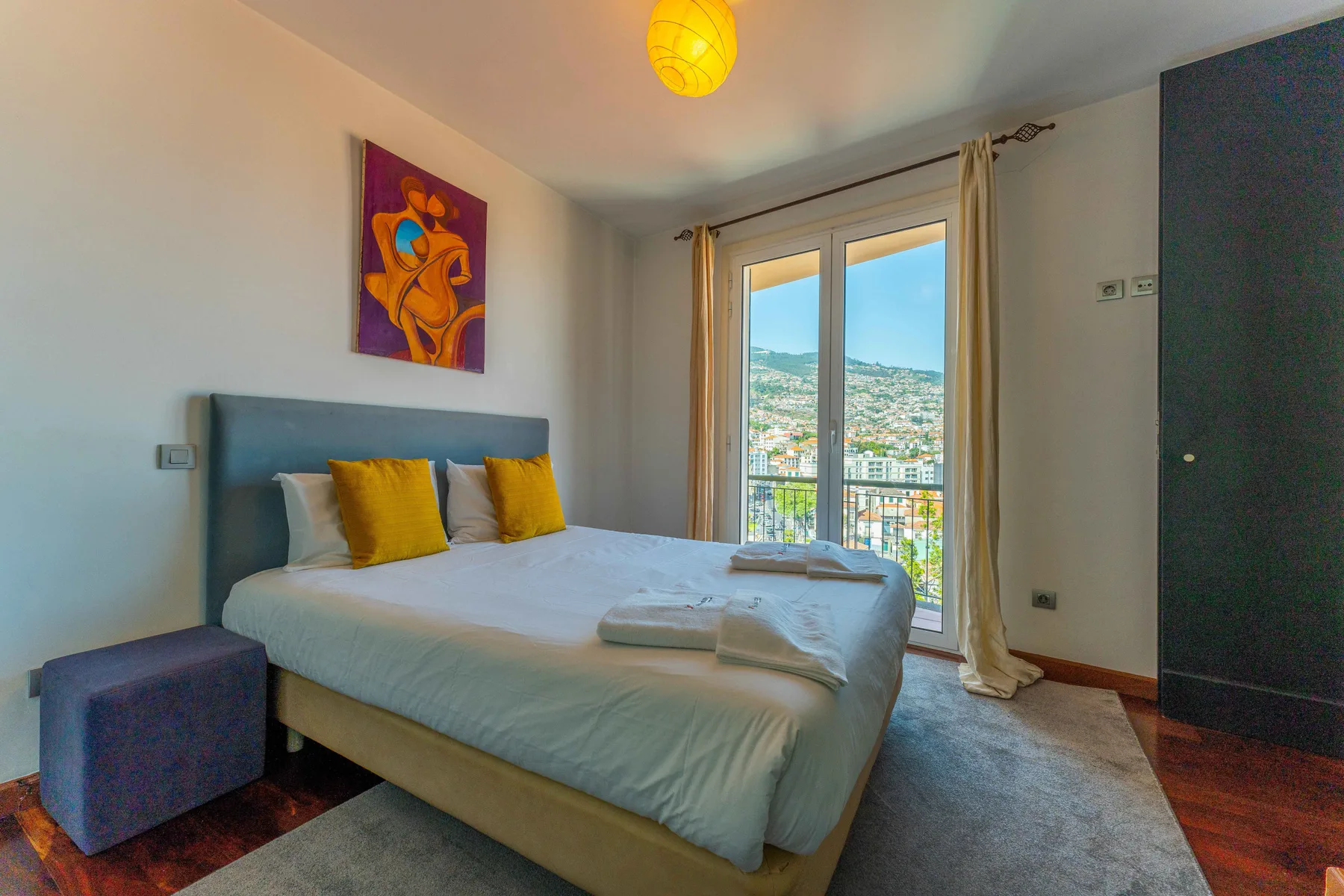 A bedroom with a bed, colorful artwork, and glass doors opening onto a balcony.