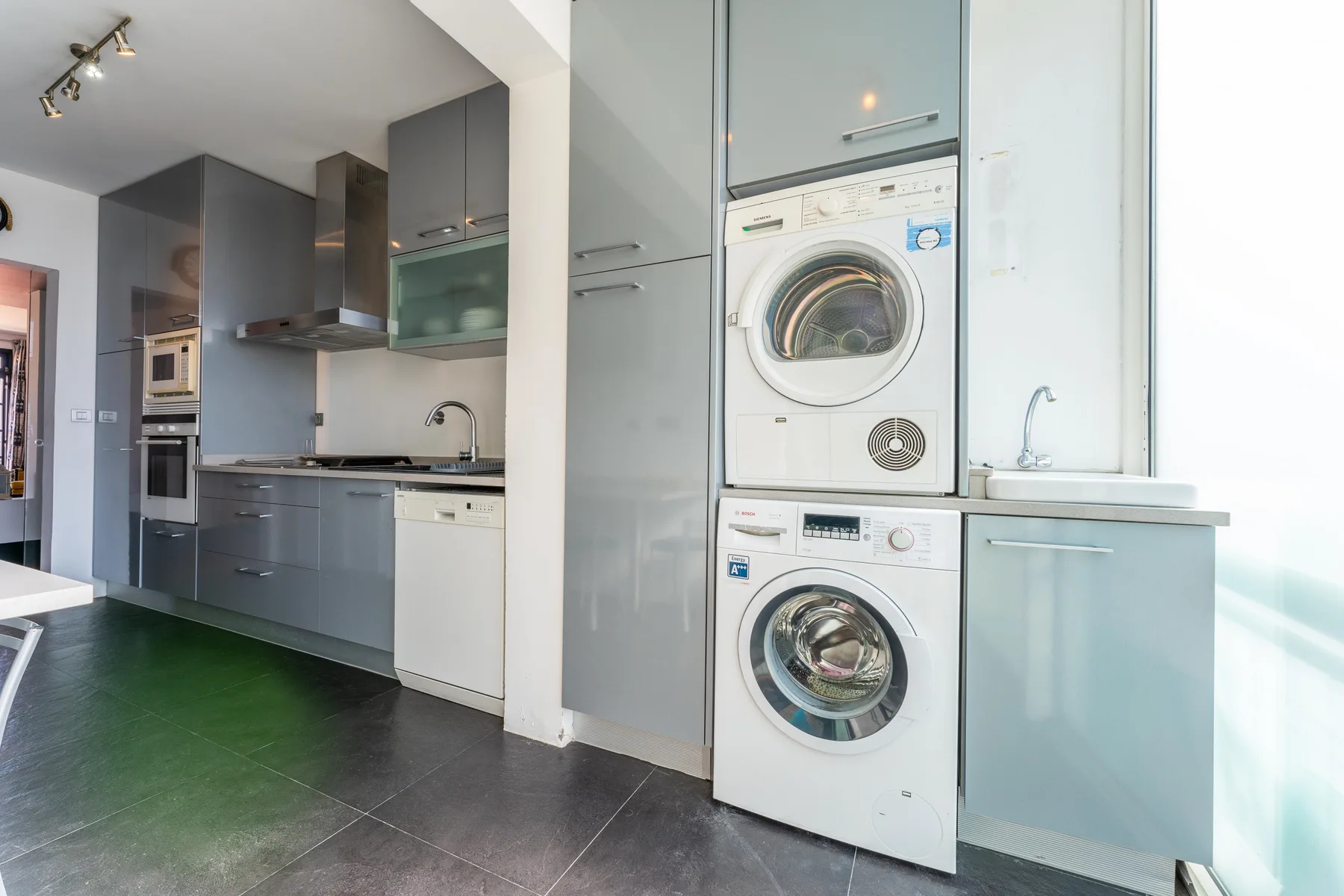 A modern kitchen with gray cabinets and stacked laundry appliances.