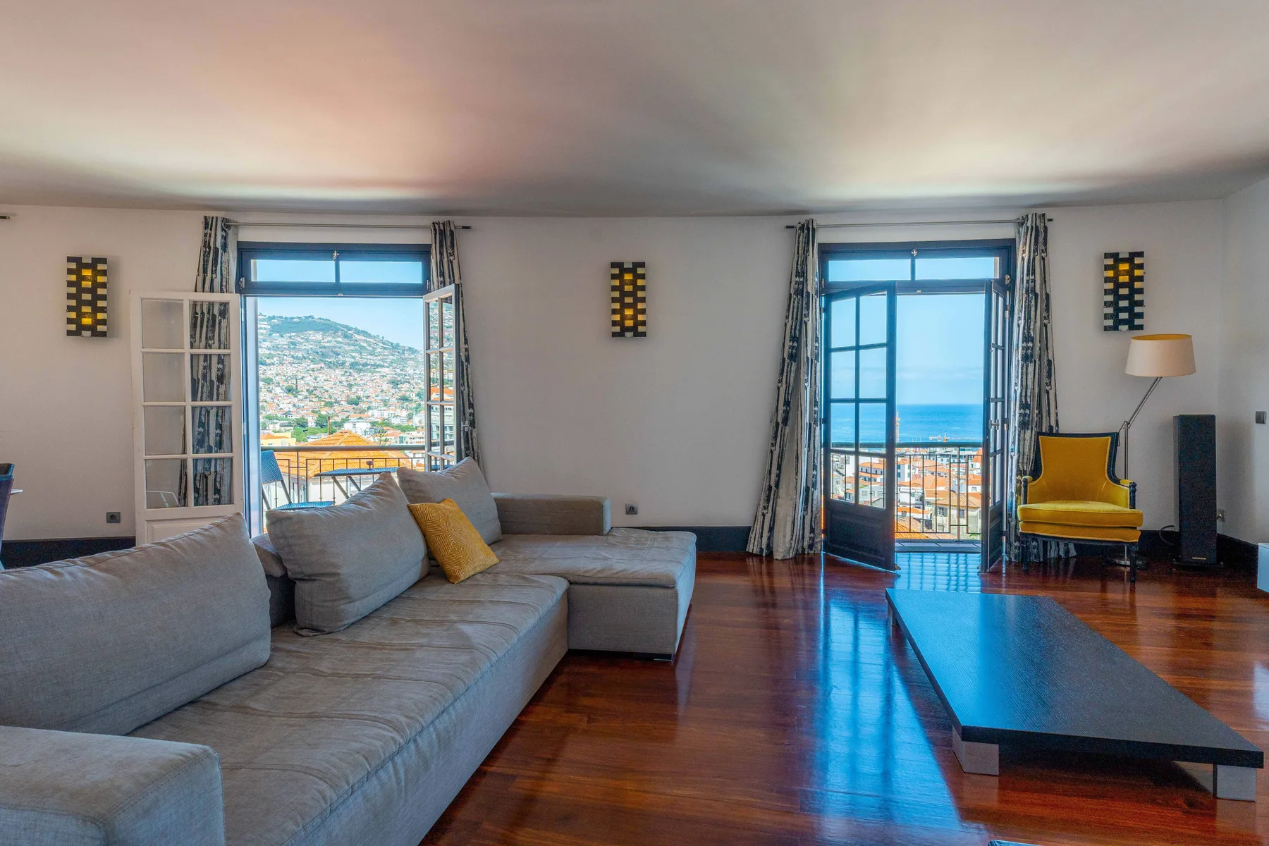 A living room with a large seating area and two open balcony doors.