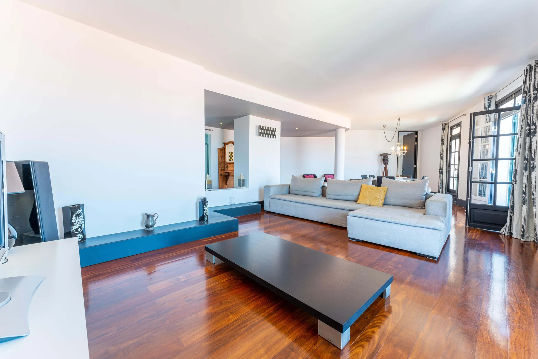 Una sala luminosa tiene un sofá seccional, una mesa de centro baja y grandes ventanas.