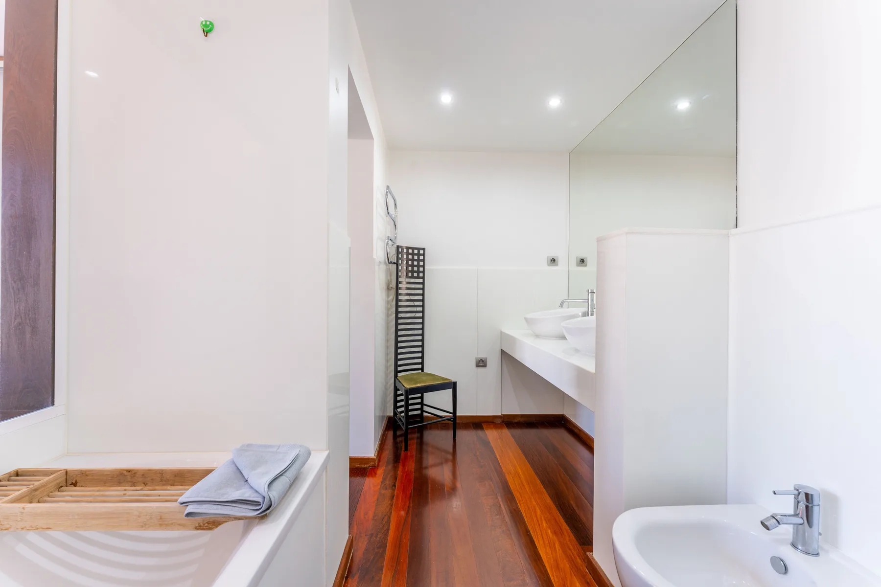 A bright bathroom with a long sink counter and a wooden floor.