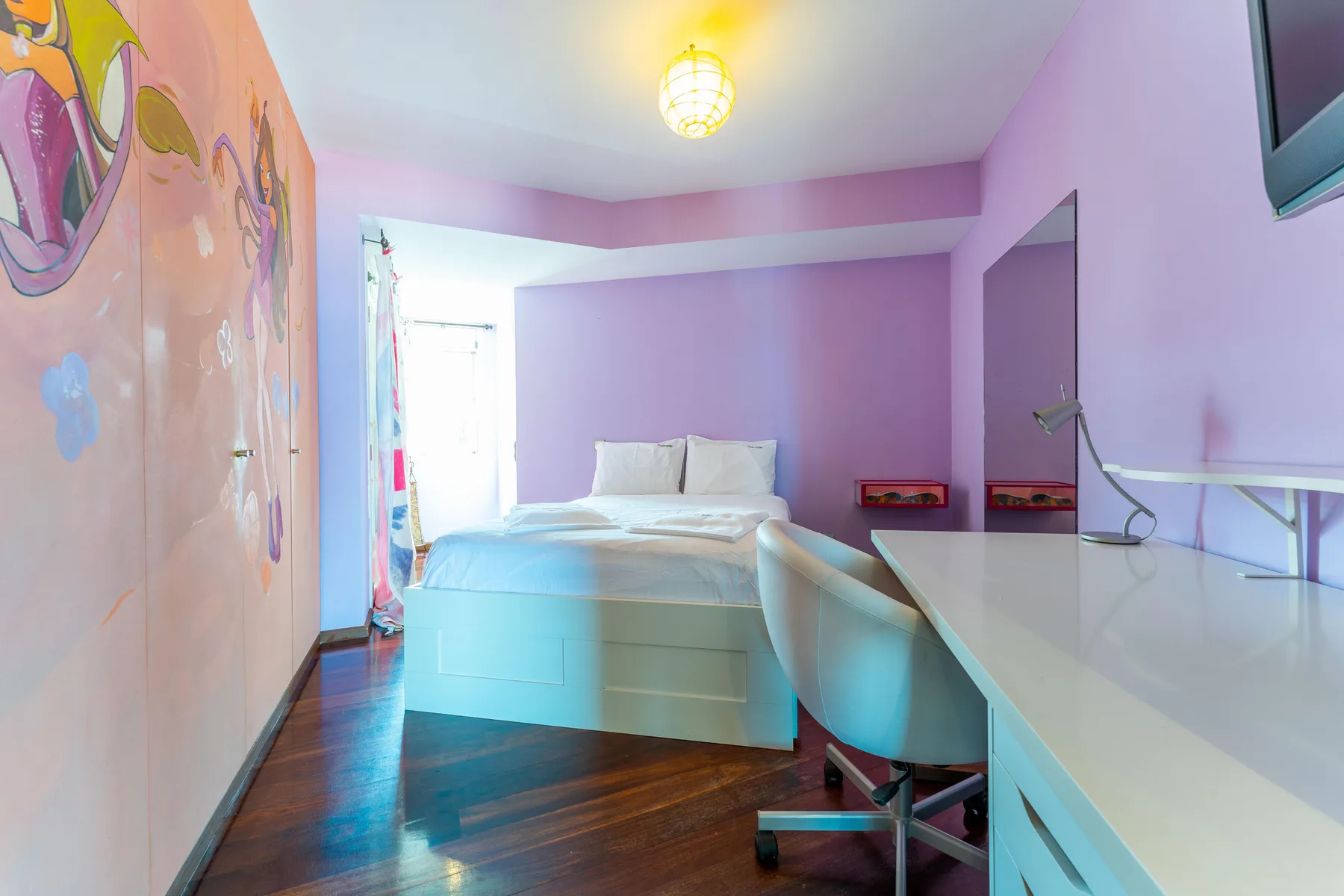 A bedroom with a bed, a desk, and colorful wall art.
