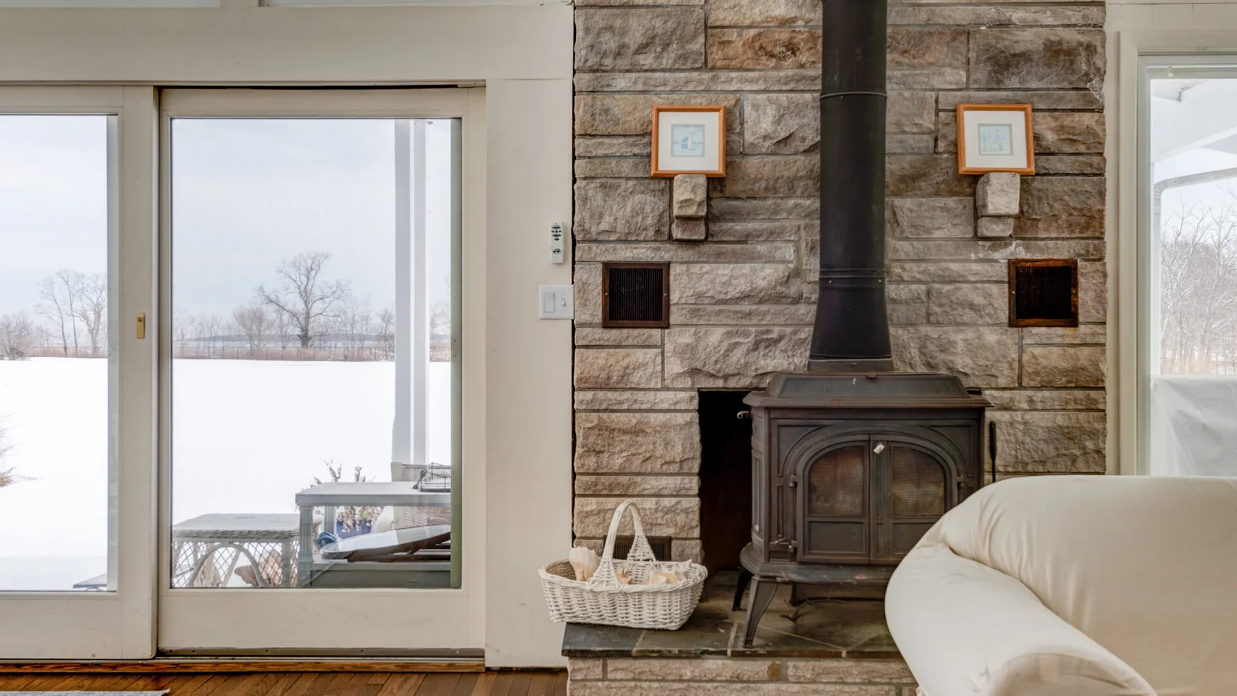 A living room with a wood stove beside large windows overlooking a snowy landscape.