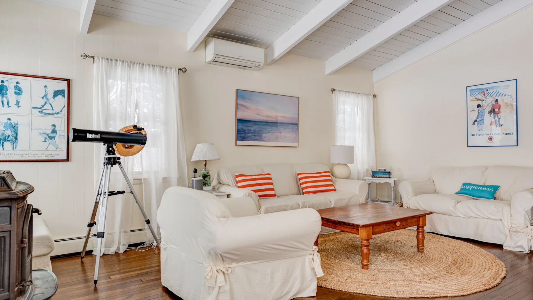 A bright living room with white seating, a wooden coffee table, and a telescope.