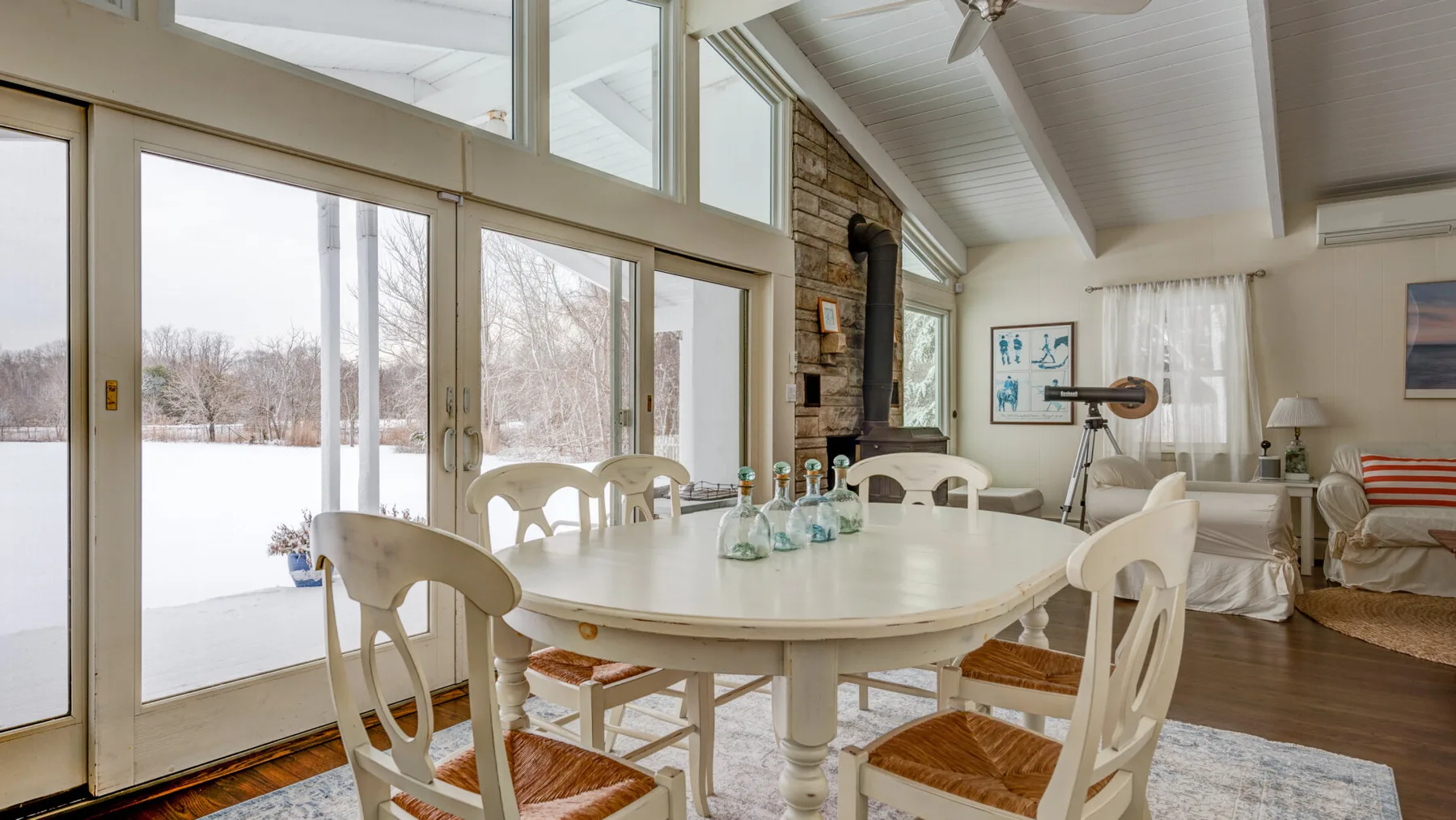 A bright dining area with a large table beside tall windows overlooking a snowy landscape.
