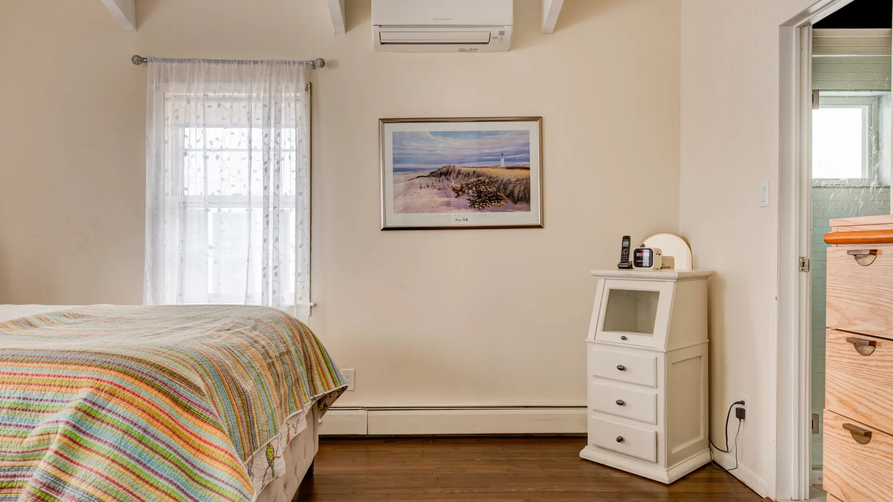 A bedroom with a striped bedspread, a curtained window, and framed wall art.