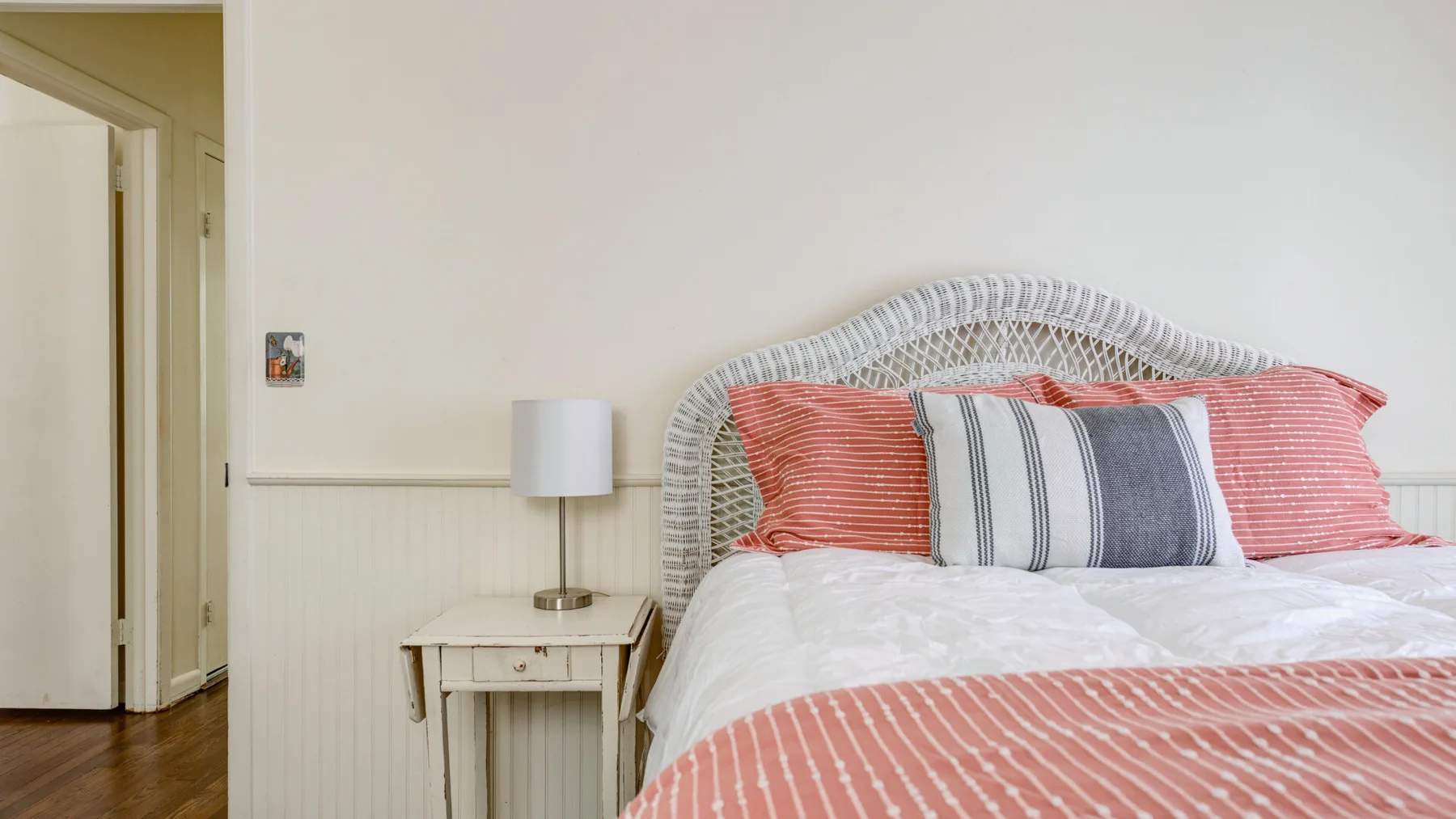 A bedroom with a bed dressed in coral and striped bedding.