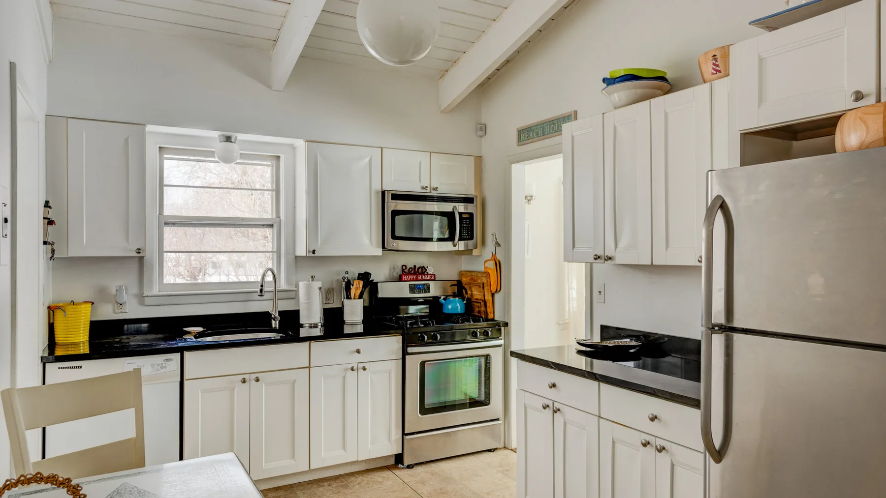 A bright kitchen with white cabinets, dark countertops, and a window above the sink.
