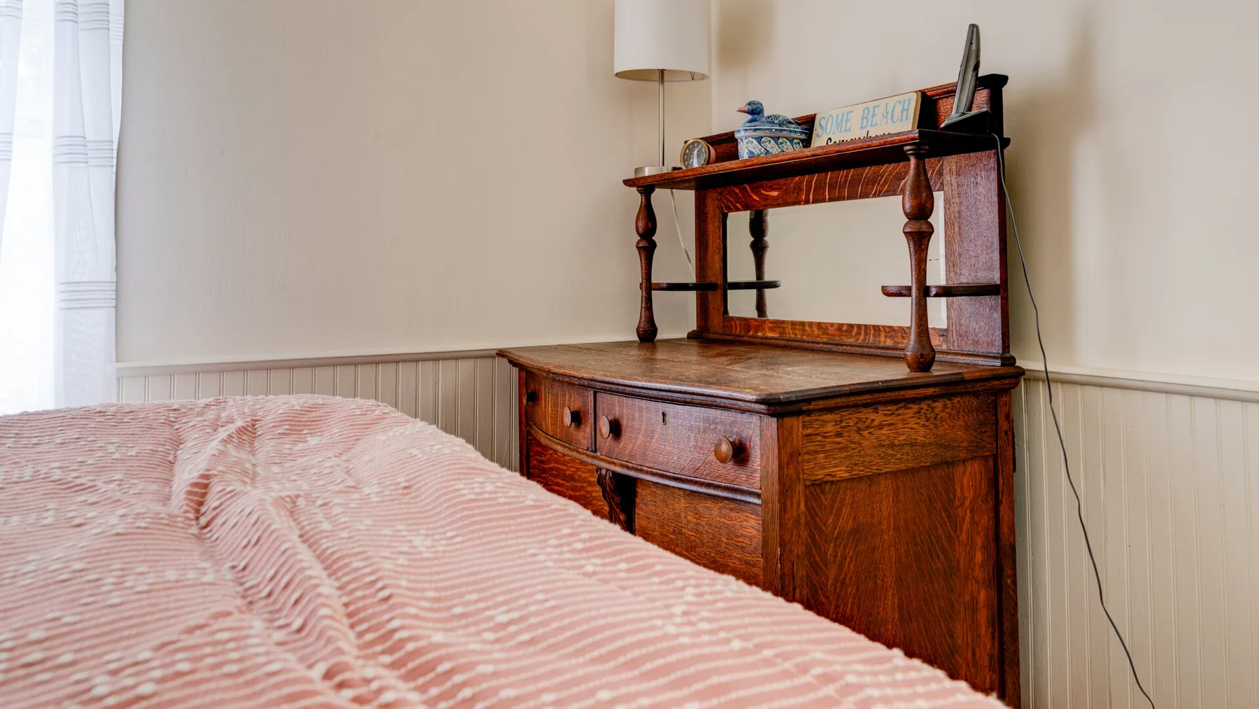 A bedroom with a bed beside a wooden dresser and shelving.
