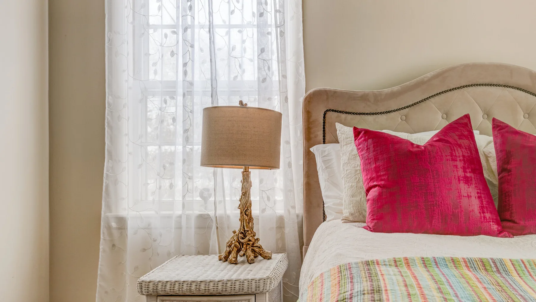 A bedroom with a bed dressed in bright pink pillows beside a curtained window.